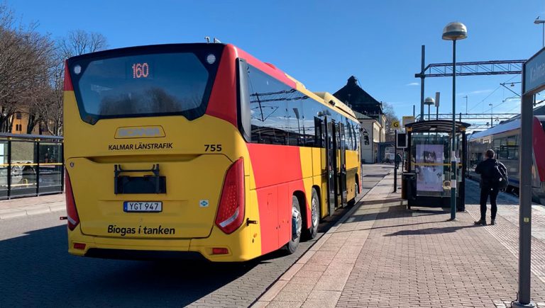 Bild tagen på en buss tillhörande Kalmar Länstrafik bakifrån. Bussen har numret 160. Bredvid bussen kan man se busshållsplatsen, tågstationen och en man som står på perrongen.