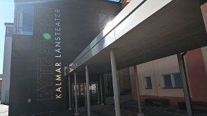Byteaterns huvudentré. Entrédörrarna syns i bild och bredvid står det "Byteatern Kalmar Länsteater". Det är en svart byggnad.
