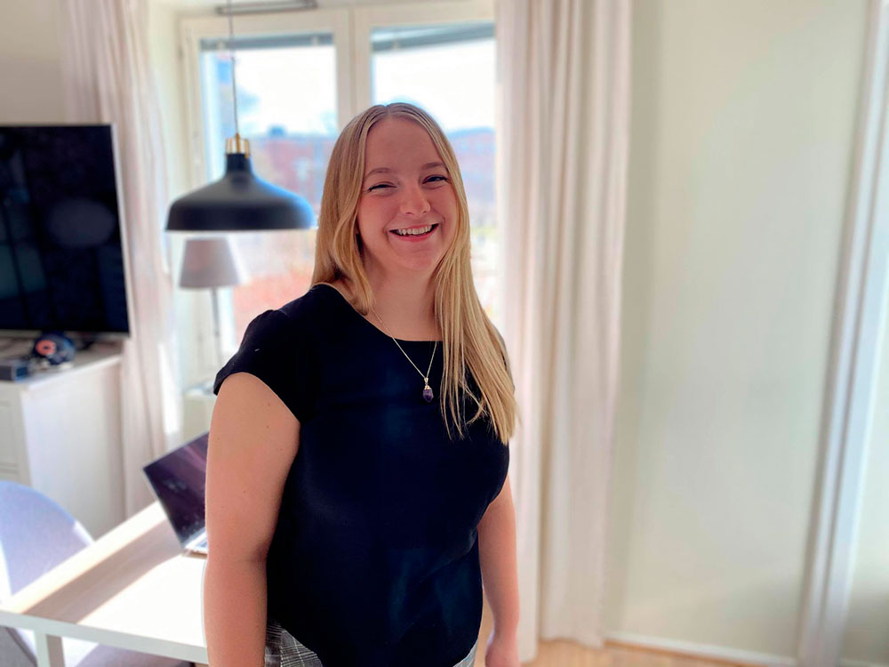 Halvbild på Filippa. Hon ler stort mot kameran och har en svart t-shirt på sig. Bilden är tagen hemma hos henne.