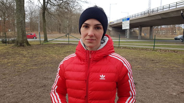 Tasha Stranda syns framifrån med ett snett leende. Hon har på sig en röd jacka och en svart mössa. Hon står i hundrastgården i Funkabo i Kalmar.