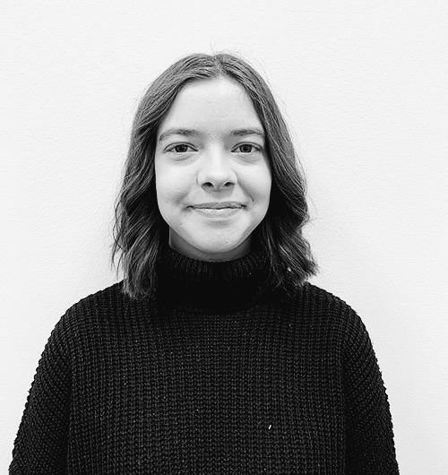 Porträttbild på Simone. Hon ler mot kameran och har en svart stickad tröja på sig. Bakgrunden är vit.