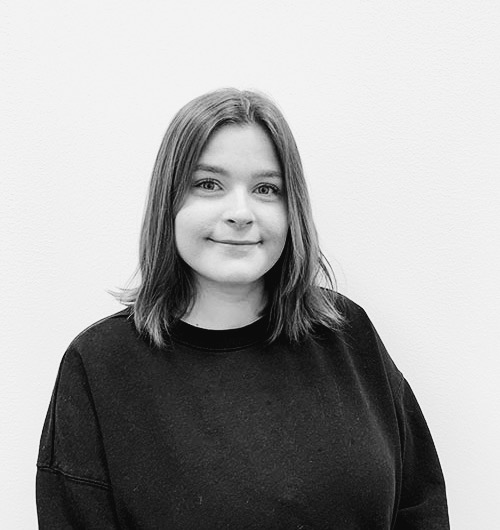 Porträttbild på Elsa. Hon ler mot kameran och har en svart tröja på sig. Bakgrunden är vit.