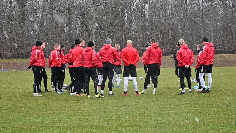 Kalmar FF står samlad i en ring under träningen på förmiddagen. Snöflingor syns falla runt laget i bilden.