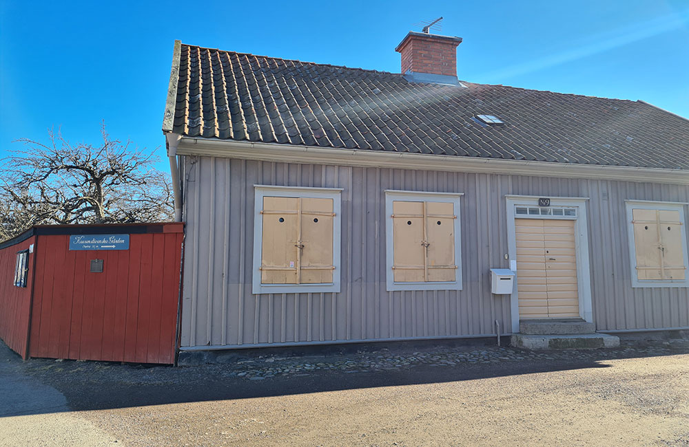 Bild på den krusentiernska gården. Ett grått hus med svart tak. Dörren och fönstren är gula.