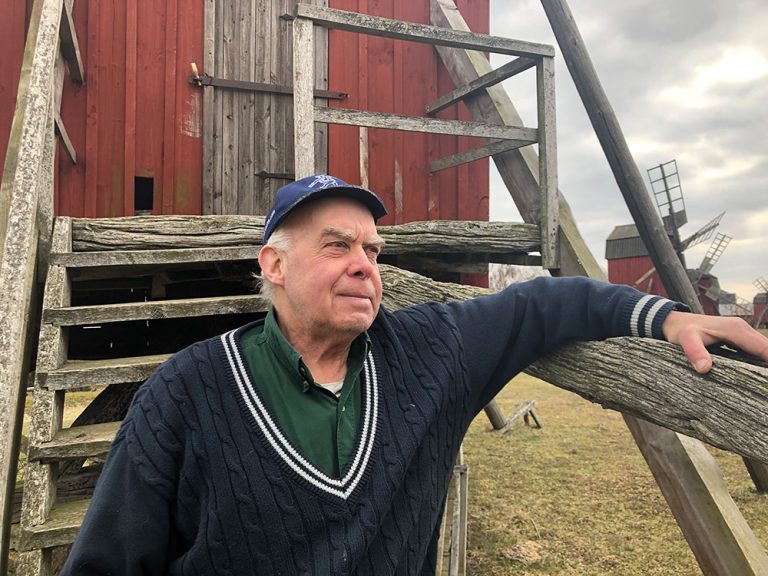 Conny Johansson ståendes vid väderkvarnarna i Störlinge. Han har en blå tröja på sig. På huvudet har han en blå keps.