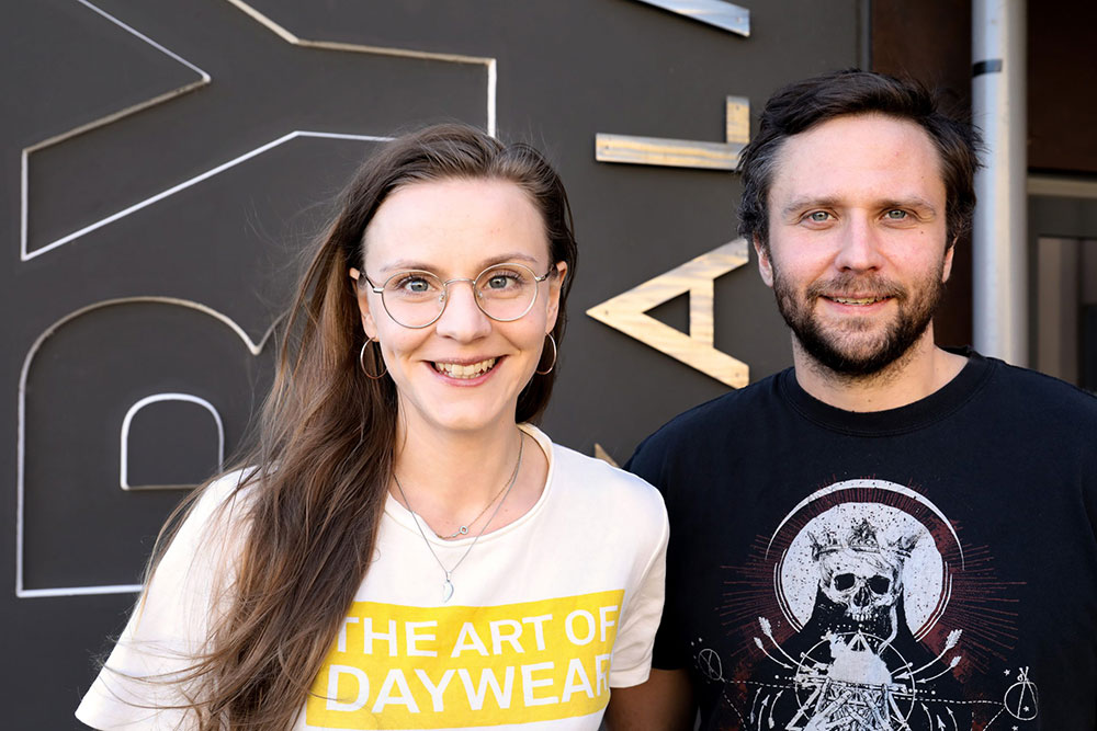Bild på skådespelarna Agnes Hargne Wallander och Edvin Bredefeldt. De står bredvid varandra och ler in i kameran. Agnes har en vit t-shirt med gult tryck på och Edvin har en svart t-shirt med vitt tryck.