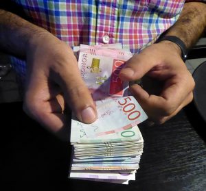 En man håller i svenska pengasedlar. Högst upp syns en femhundring. Endast mannens händer och sedlarna syns i bild.