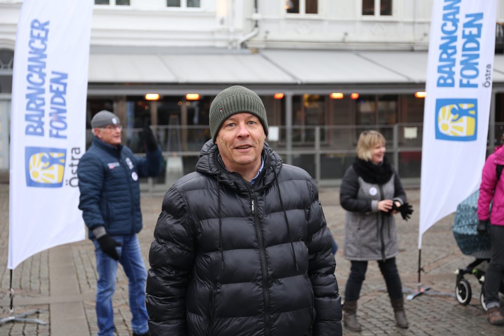 Arrangören Åke Jonsson med föreningskollegorna och Barncancerfondens flaggor i bakgrunden.