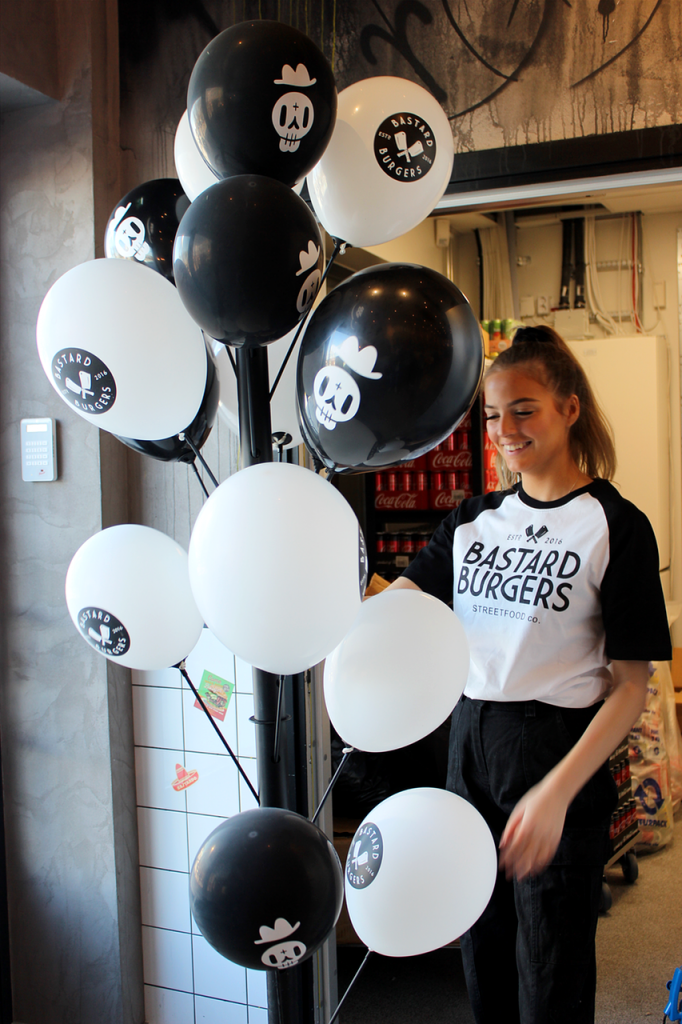 En tjej som jobbar på Bastard Burgers står bredvid ett ställ med svarta och vita ballonger.