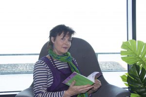 Bild på en Catte Jern som sitter i en fåtölj och läser ur sin diktbok.