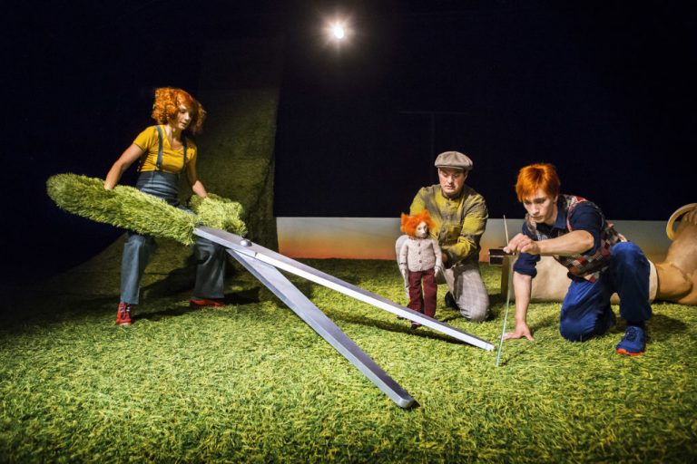 Bild från en föreställningen Gräs där en av skådespelarna klipper gräset med en sax som är större än henne själv.