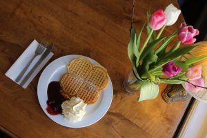 En våffla med sylt och grädde på ett bord med en bukett tulpaner bredvid.