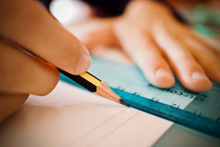 Närbild på hand som drar ett streck med blyerts efter linjal