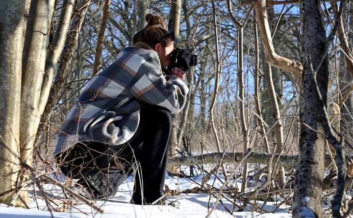 Bild på intervjupersonen som sitter på snö i skogen och fotograferar