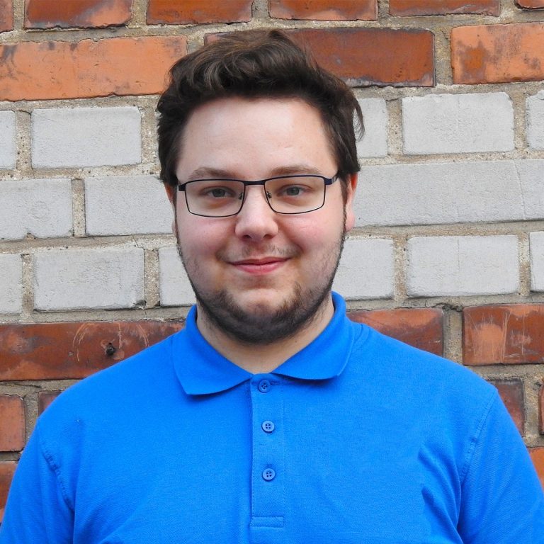 Alexander Finstad står iklädd blå tröja och ler.