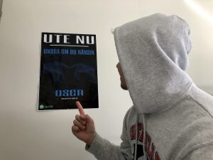 Oscar står med ryggen mot kameran och pekar på en poster på en av hans låtar.