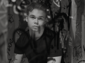 Osscar sitter framför en badrumsspegel som är målat på med svart sprayfärg och kollar in i kameran.