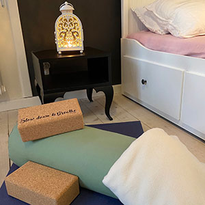 En yoga matte med redskap på och en ljuslykta står bredvid en säng