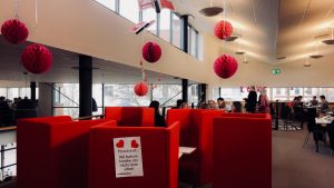 Bild på röda soffor i biblioteket. På en av sofforna sitter det en lapp som lyder "Pssst. Här bakom kanske din nästa date sitter!". I taket hänger det ner röda dekorationer med anledning av alla hjärtans dag.