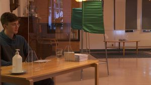 Ett valbås står i mitten av en vallokal. En person sitter vid ett bord bredvid.