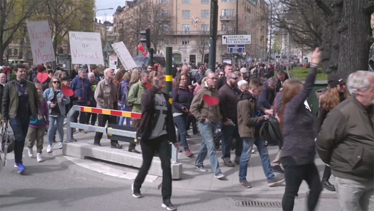 Många människor som går med skyltar i demonstration mot vaccin