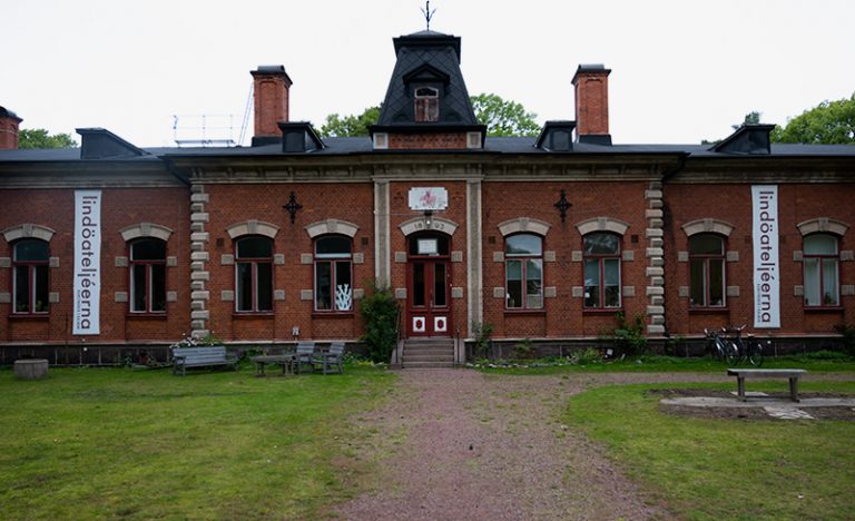 Ett stort, dekorativt hus i rött tegel med Lindöateljeerna-skyltar