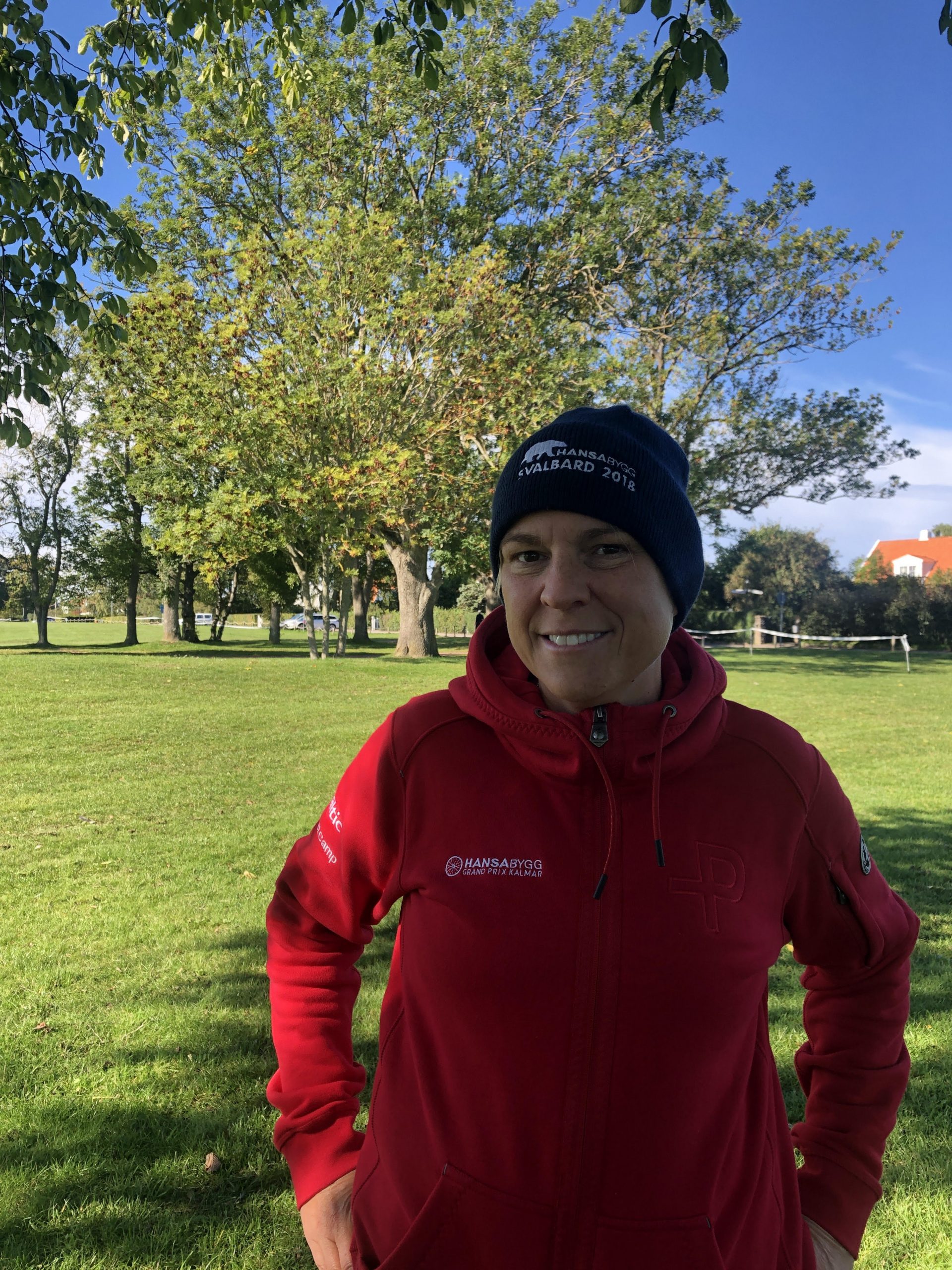 Kvinna i röd tröja står i grönskande miljö