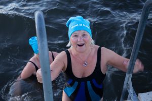 Lisa Vikestam ler när hon klättrar upp på stegen efter att ha kallbadat i havet. Hon har baddräkt och en blå mössa på sig, där det på mössan står: "Badare är gladare"