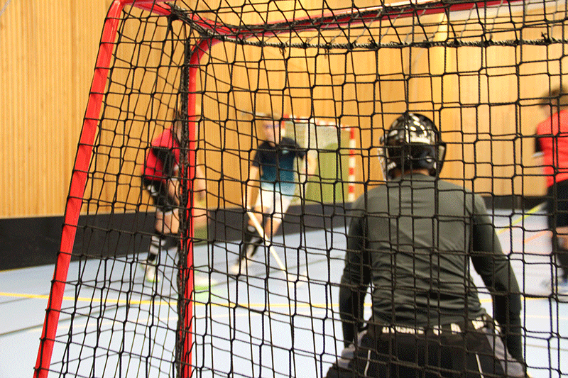 Bakom ett innebandymål, spelare ur fokus i bakgrunden