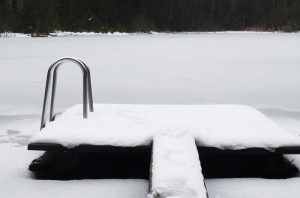 Snöig brygga med stege. Vattnet är fryst till is och täckt med snö.
