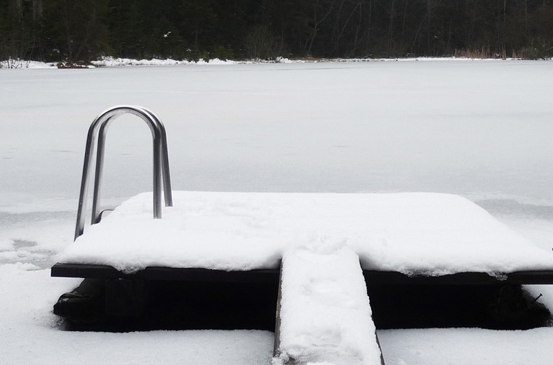 Snöig brygga med stege. Vattnet är fryst till is och täckt med snö.