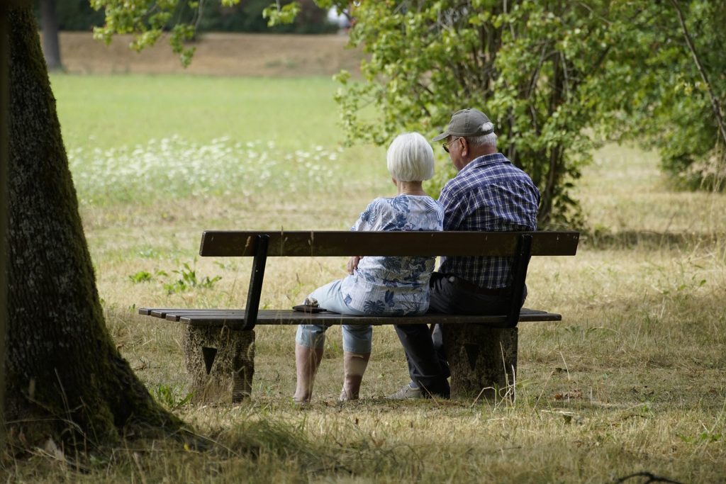 Två pensionärer sitter på en bänk i en park.