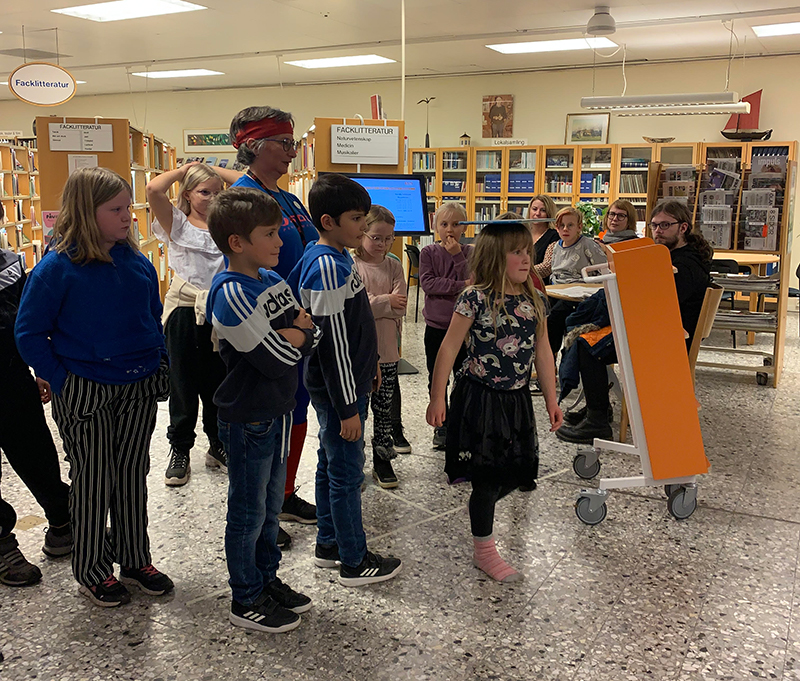 Barn balanserar böcker på huvudet.