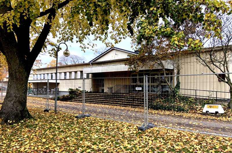 Träd framför byggnaden som är omringa av staket