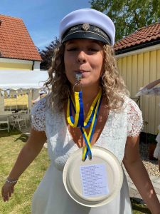 Elsa Persson står i sin studentmössa och visslar i sin visselpipa