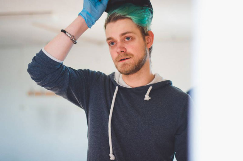 En man med blå hoodie och grönt hår lyfter sin hatt.