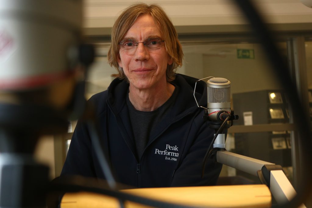 Joakim Johansson står i radiostudion och ler in mot kameran.