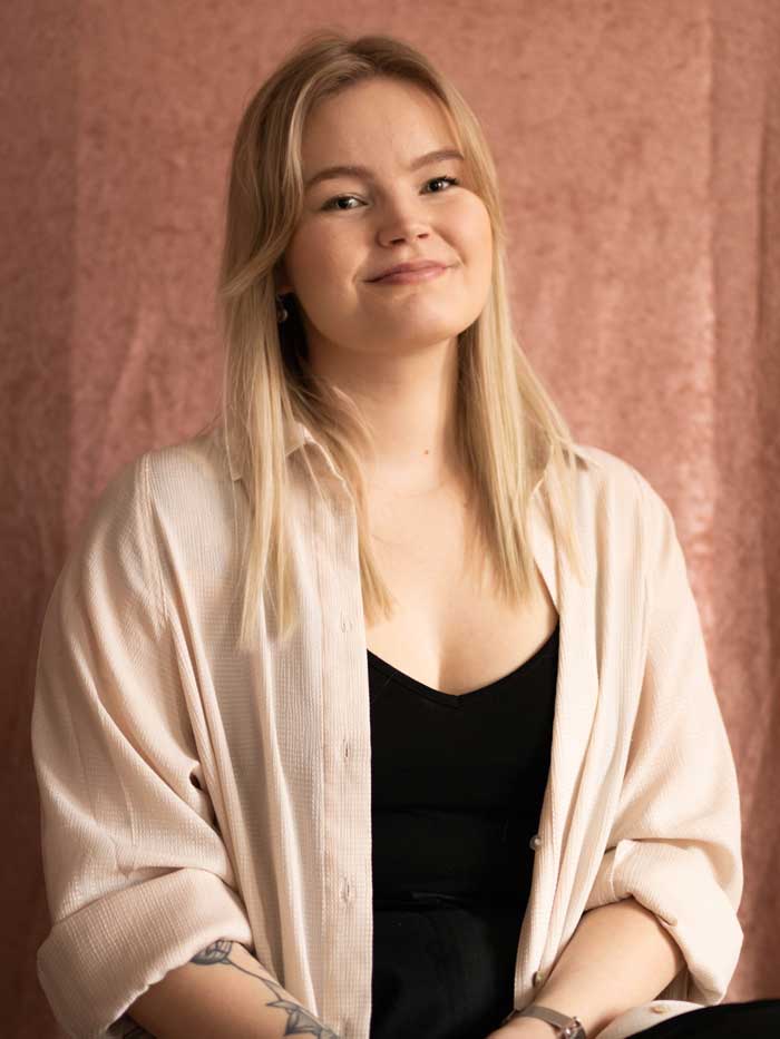 Reporter Linda framför en rosa bakgrund.