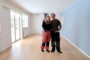 En tjej med rosa arbetsbyxor och en kille med svarta arbetsbyxor. En blå vägg och ett tomt rum.