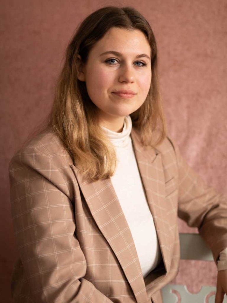 Reporter Paula framför en rosa bakgrund.