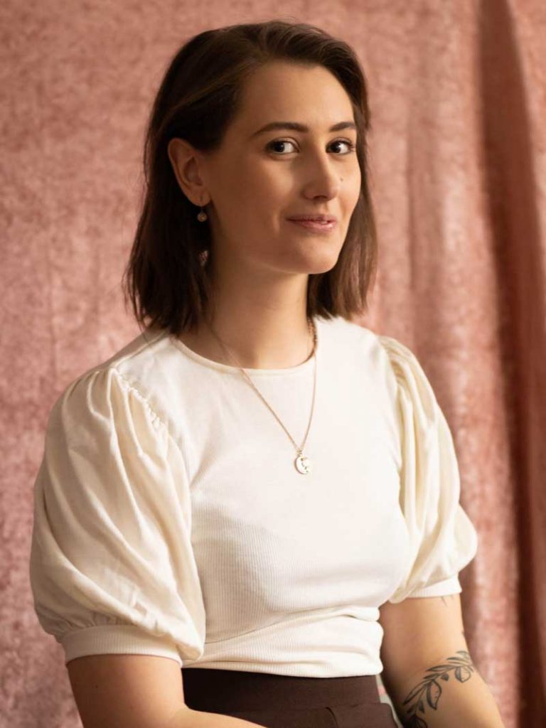 Reporter Tess framför en rosa bakgrund.