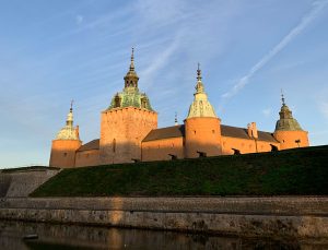 Ett ljusbrunt stort slott med fyra spetsiga torn. En vallgrav runtom.