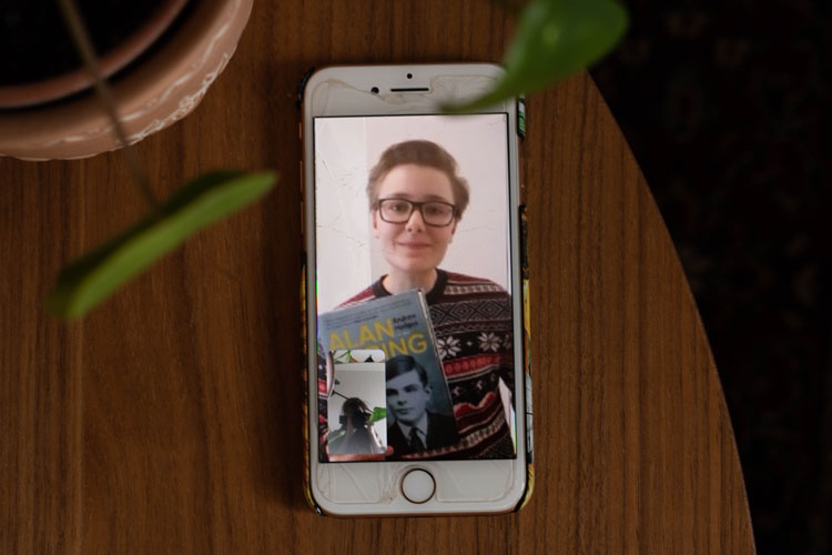 En kille på en mobil som håller i en bok. Två gröna blad i förgrunden.